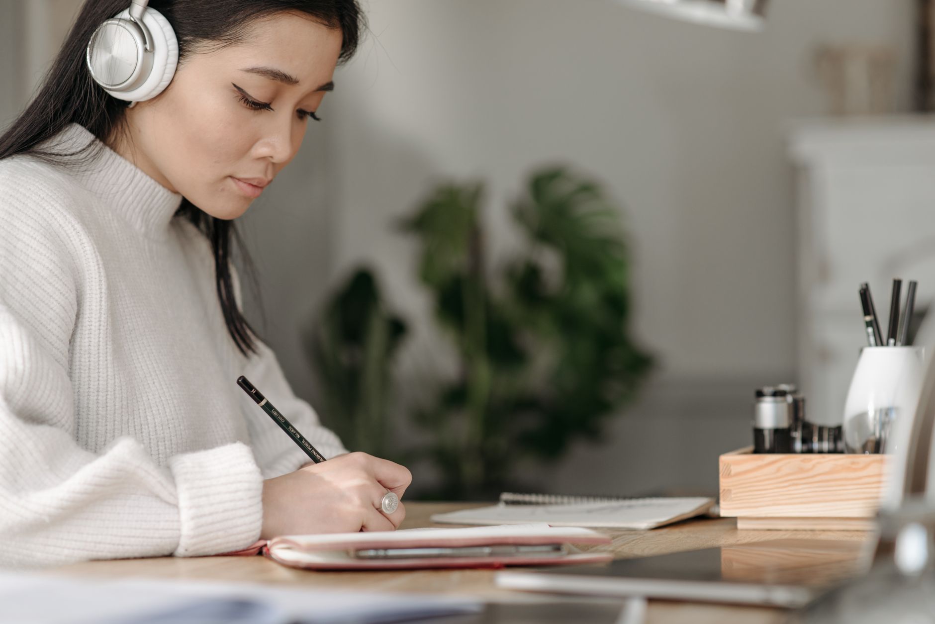 Aluna de inglês com fones de ouvido anotando no caderno quanto entendeu do áudio
