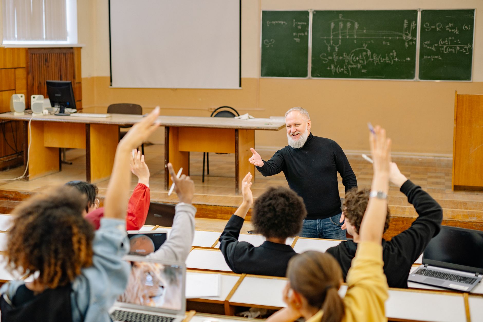 Professor em sala de aula com alunos participando de mãos levantadas
